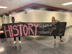 two women holding a sign that says history repats are here in front of them