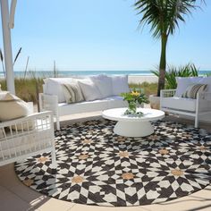 an outdoor living area with white furniture and palm trees on the beach in the background