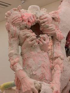 a sculpture is covered in pink and white paint, with hands on the face as if it were holding something