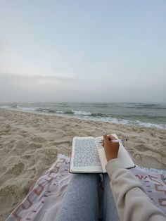 a person sitting on top of a beach next to the ocean with a laptop computer