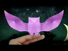 a hand holding an origami bird in front of the moon