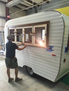 a man standing next to a white trailer in a garage with windows on each side