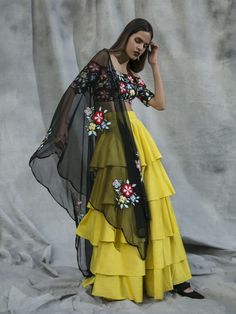 This vibrant set features a black off shoulder blouse in silk and net base with cutdana and multi-coloured thread hand embroidered floral motifs. It is paired with a yellow ruffles tiered lehenga skirt and a black net dupatta. Yellow Lengha, Amrit Kaur, Tiered Lehenga, Ruffle Lehenga, Blouse Designs Silk, Lehenga Skirt, Black Off Shoulder, Yellow Skirt, Net Dupatta