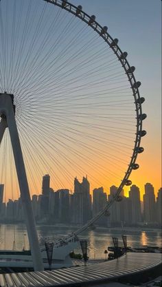 a ferris wheel in front of a large cityscape with the sun setting behind it