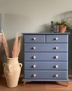 a blue dresser sitting next to a vase with some plants on top of it in a room