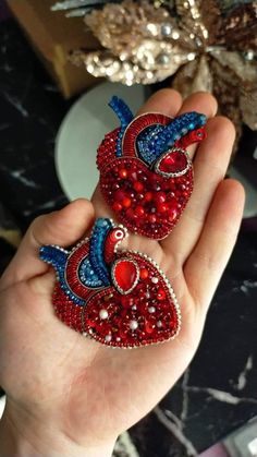 two red and blue bird brooches are in someone's hand on a table