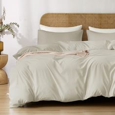 an unmade bed in a bedroom with white walls and wood flooring, along with wicker headboard