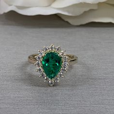 a close up of a ring with a green stone in the middle and white flowers behind it