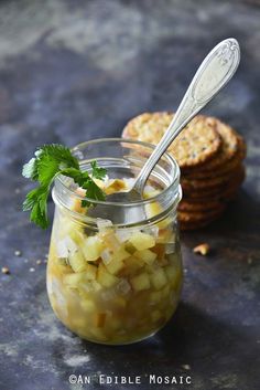 a glass jar filled with pickled vegetables next to crackers and a spoon on a table