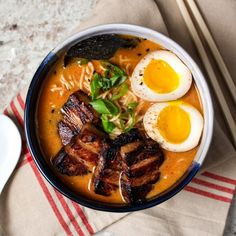 a bowl of ramen with meat, eggs and noodles on a napkin next to chopsticks