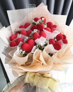 a bouquet of red and white flowers in someone's hand with ribbon around it