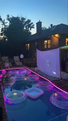 an outdoor pool is lit up with purple lights and floating bowls in the foreground