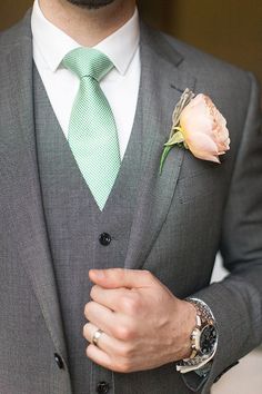 a man in a gray suit with a green tie and flower boutonniere