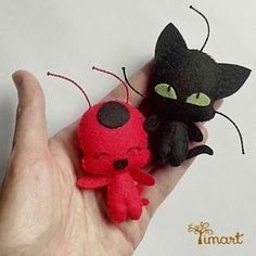 a hand holding two small stuffed animals in it's palm, one is black and the other is red