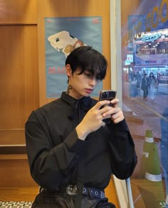 a young man sitting down looking at his cell phone in front of a store window