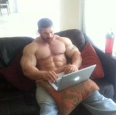 a shirtless man sitting on a couch using a laptop computer