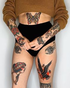 a woman with many tattoos on her body and legs, standing in front of a white wall