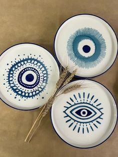 three blue and white plates with an eye design on them, one has a stalk in front of it