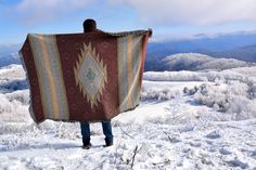 a man standing on top of a snow covered hill holding a blanket over his head