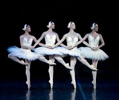 four ballerinas in white tutus are standing on stage