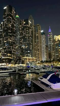 boats are docked in the water near some tall buildings at night with lights on them