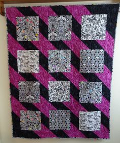 a pink and black quilt hanging on a wall