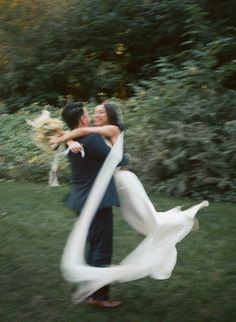 a bride and groom are hugging in the grass