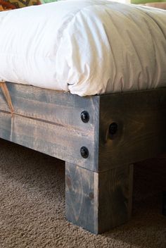 a wooden bed frame sitting on top of a carpeted floor next to a white pillow