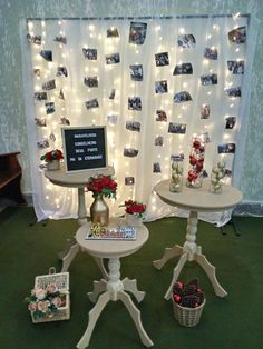 two white tables with flowers and pictures on the wall behind them are decorated with string lights