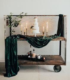 a wedding cake sitting on top of a wooden table next to a green drape