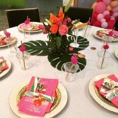 the table is set with pink and gold plates, place settings, and tropical decorations