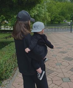 a woman holding a child in her arms while standing on a brick walkway next to a park