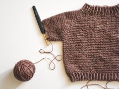 a knitted sweater and ball of yarn next to a crochet knitting needle