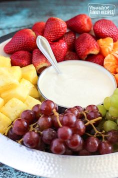 a white bowl filled with lots of different types of grapes and strawberries next to a cup of yogurt