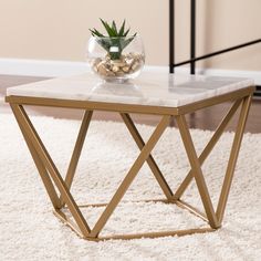 a marble top coffee table with gold metal legs and a plant in a glass vase