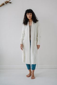 a woman standing in front of a wall wearing a white cardigan sweater and jeans