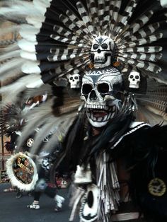 a man with skull makeup and headdress in front of a large group of people