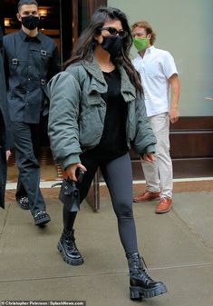 a woman in black and green is walking down the street with her face covered by a mask