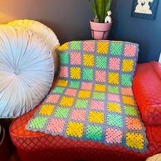 a crocheted blanket sitting on top of a couch next to a potted plant