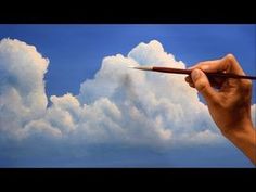 a hand holding a paintbrush in front of some clouds