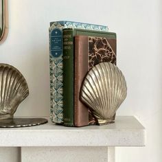 two books are sitting on a shelf next to a sea shell and a bookend