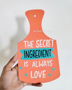 a hand holding an orange tag with the words, the secret ingredient is always love