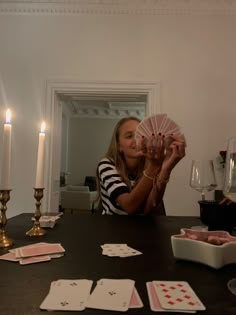 a woman sitting at a table with cards and candles in front of her holding up a pink card