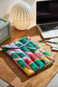 an open laptop computer sitting on top of a wooden desk next to a colorful blanket