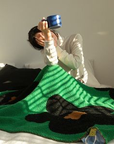 a woman laying on top of a bed covered in a blanket and holding a cup