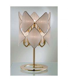 a lamp that is sitting on top of a glass table with a gold base and white lampshade