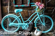 a blue bicycle with flowers in the basket next to a white duck and brick wall