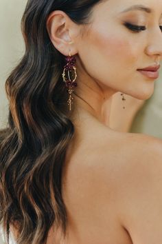 a woman with long hair wearing red and gold earring on her left side, looking off to the side