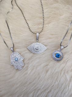 3 style evil eye necklaces.  ---- Sold separately ---- Clear cubic zirconia. Silver plated brass. Lobster clasp. Dimensions Hamsa hand: SOLD Round blue evil eye: 2.6cm height, 1.8cm width. Eye shape evil eye: 3.4cm height, 3.5cm width. CARE INSTRUCTIONS: To take care of plated jewelry, you should: 1. Avoid getting the jewelry wet with water, soap, perfume, lotion and other chemicals. If the jewelry does get wet, wipe it immediately with a soft cloth. - Do not spray on perfume or other sprays whi Silver Diamond Evil Eye Jewelry, Evil Eye Pendant Necklace In Cubic Zirconia, Evil Eye Cubic Zirconia Round Necklaces, Evil Eye Round Cubic Zirconia Necklace, Silver Diamond Evil Eye Necklaces, Silver Evil Eye Diamond Necklace, Silver Diamond Necklace With Evil Eye Detail, Blue Evil Eye, Evil Eye Necklace