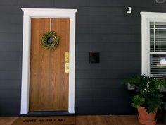 a wooden door with a wreath on it in front of a gray wall and two potted plants